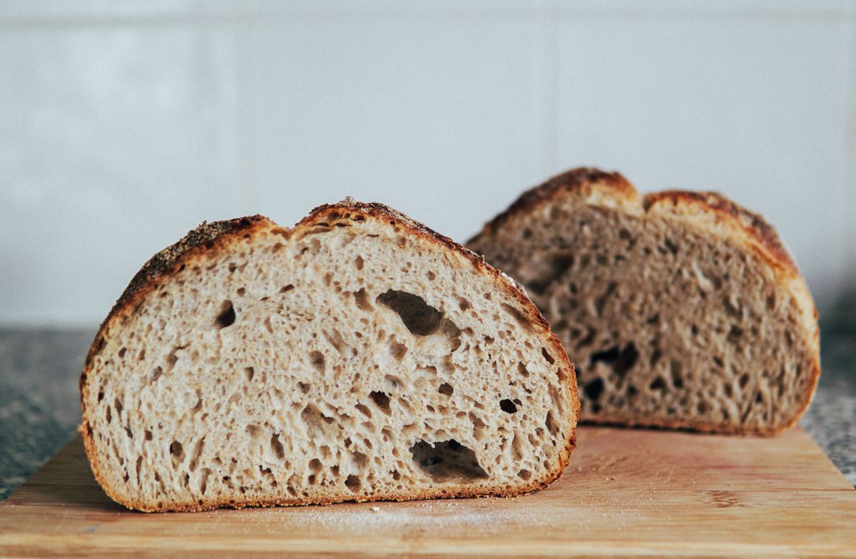 Two crusty loaves cut open on a wooden board, showing an open crumb and a dark crust