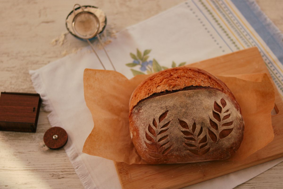 A round sourdough loaf with decorative leaf scoring on a wooden board