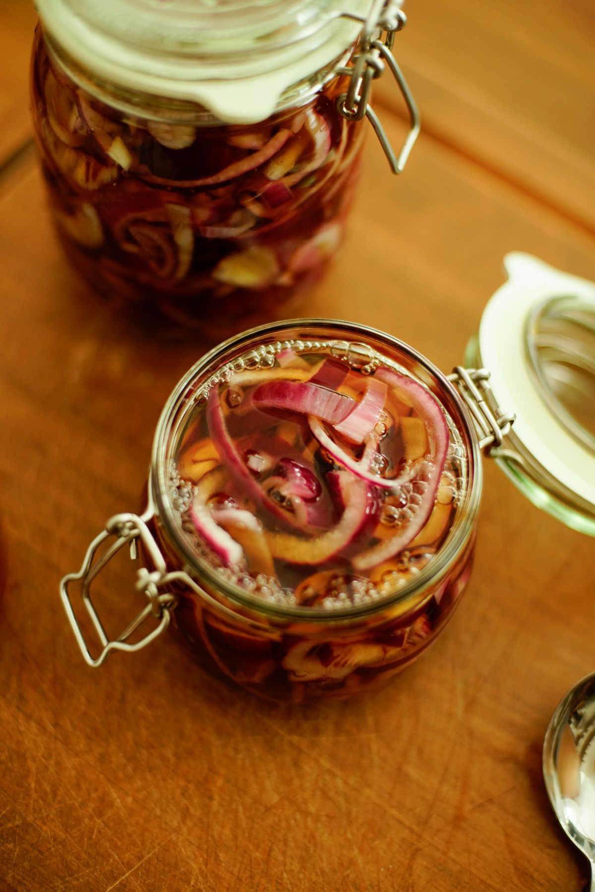 Two open jars of pickled red onion in golden brine, seen from above