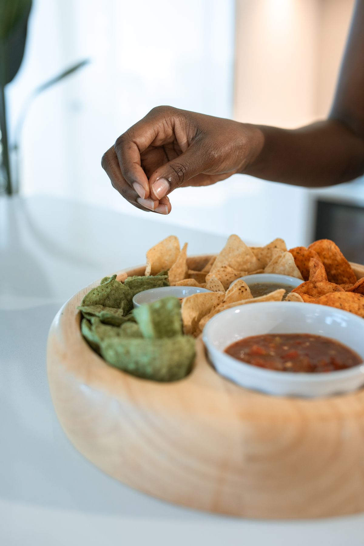 A hand reaching for tortilla chips beside a bowl of chunky salsa on a wooden serving board