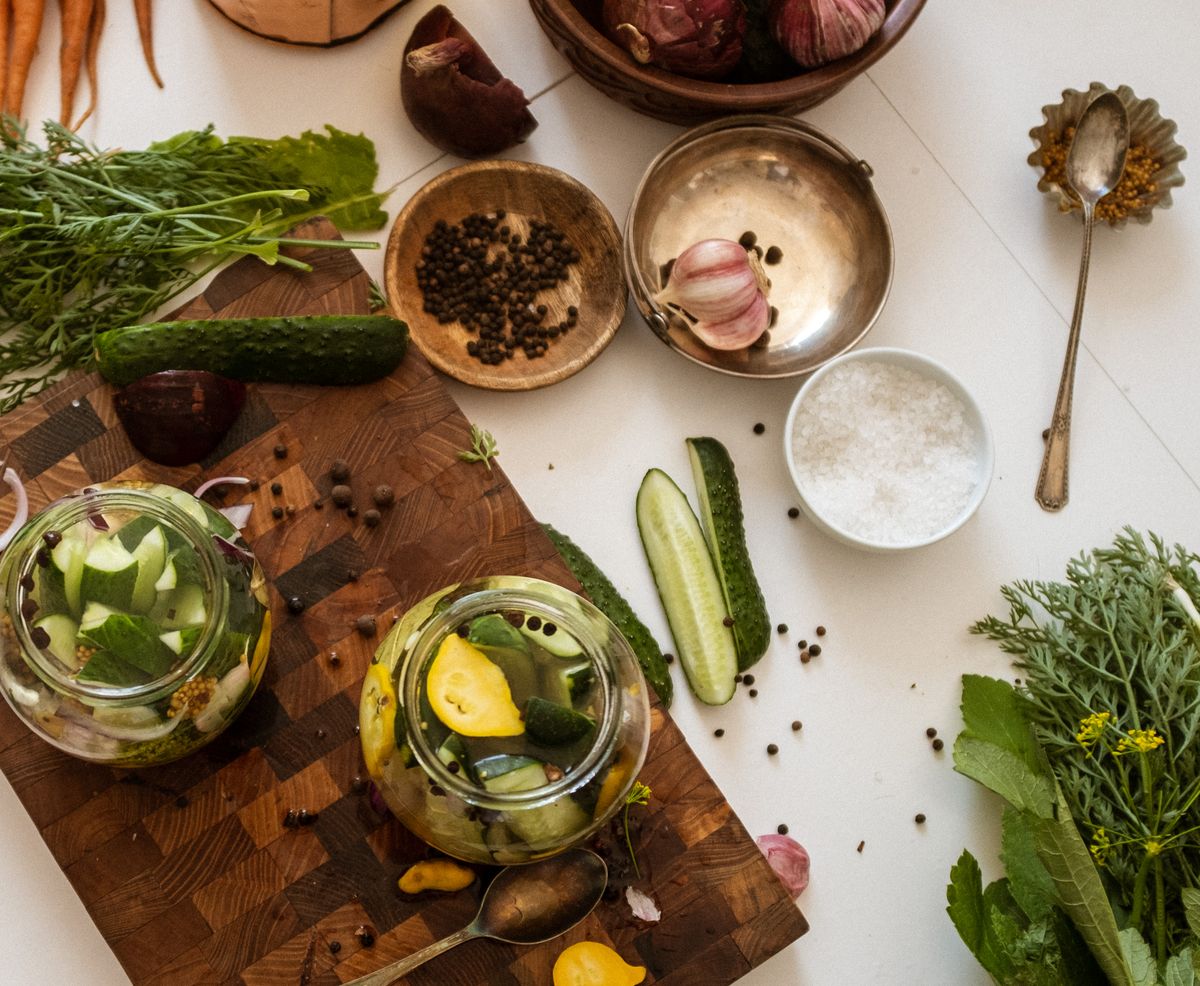 Cucumbers, dill, garlic, peppercorns and a small bowl of salt laid out on a board around two packed jars