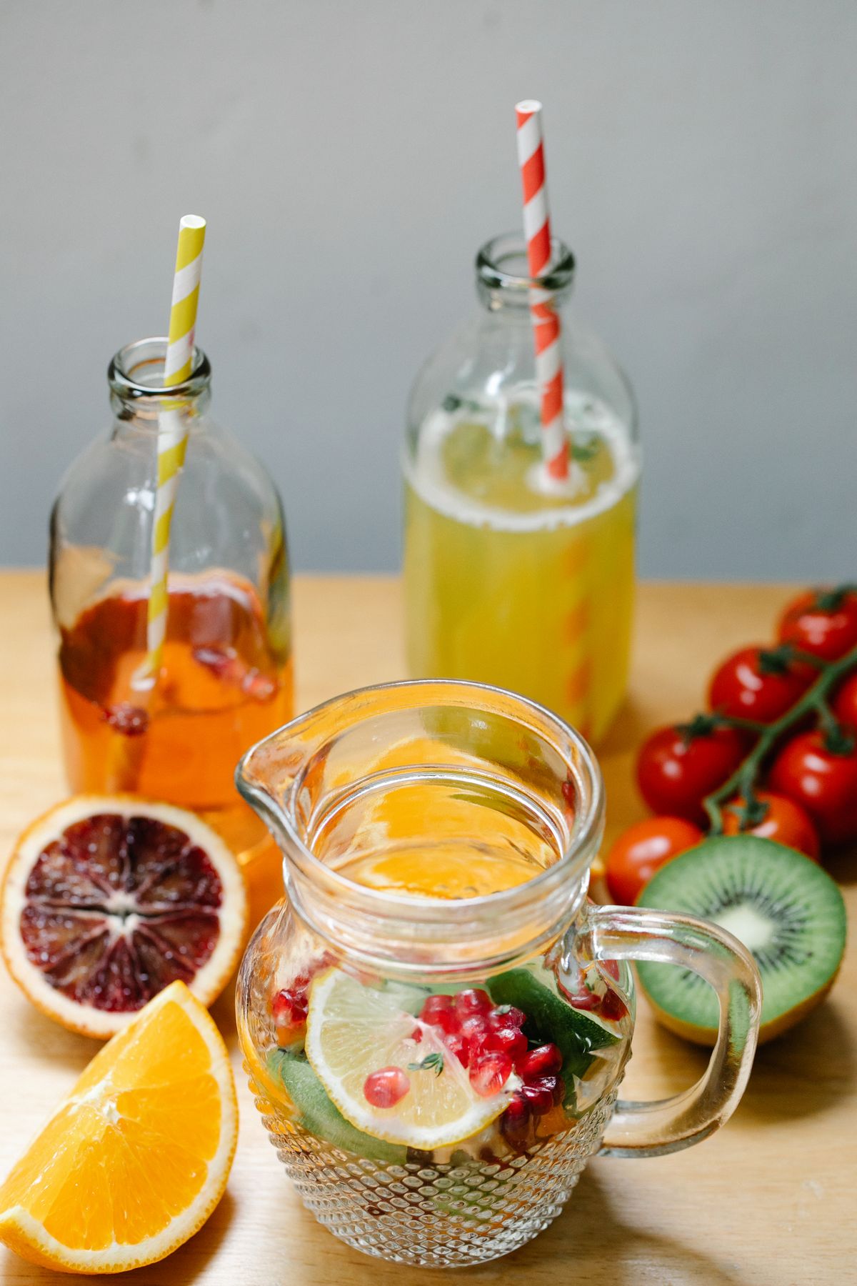 Vibrant glass pitcher and bottles with fruit-infused drinks, kiwi, orange and berries