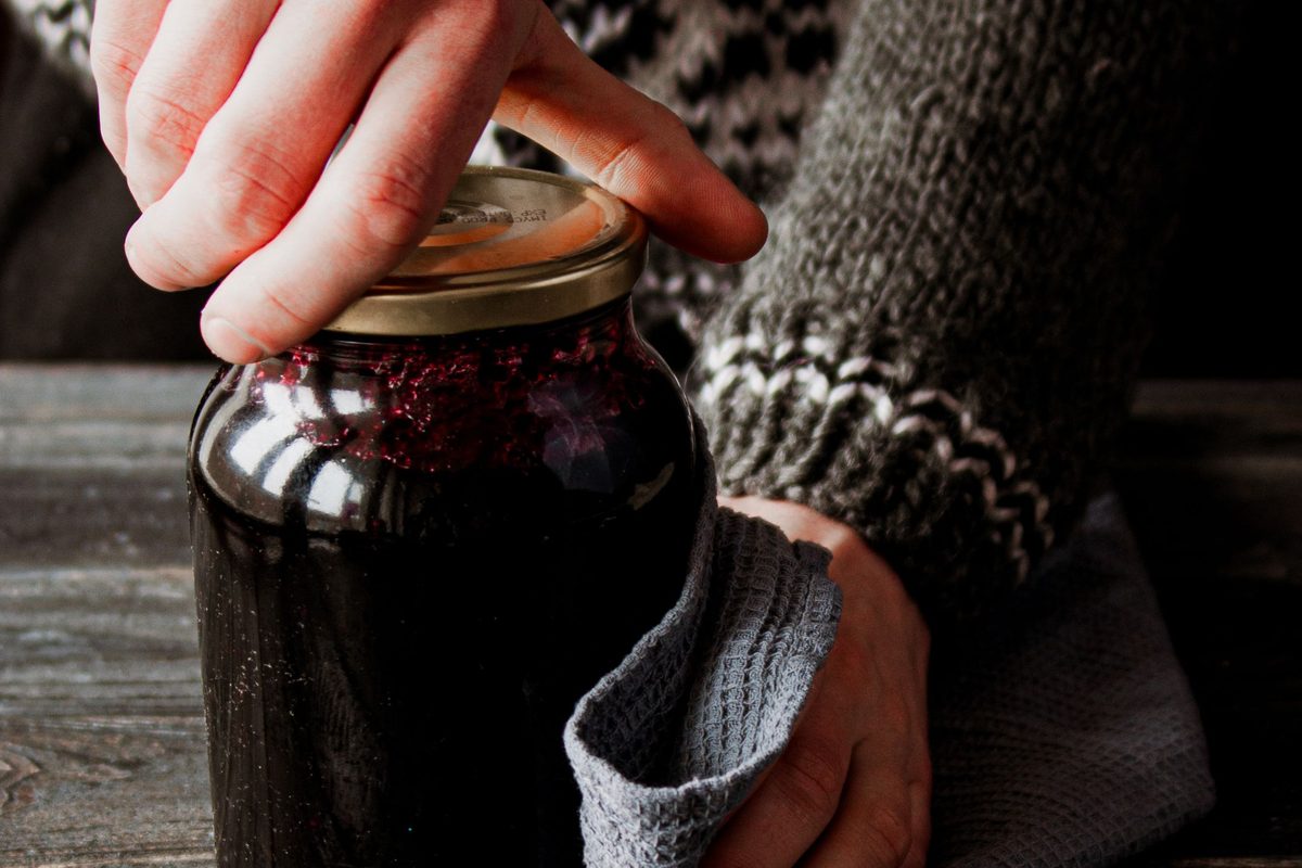 Hands twisting open a jar of dark preserves on a rustic table