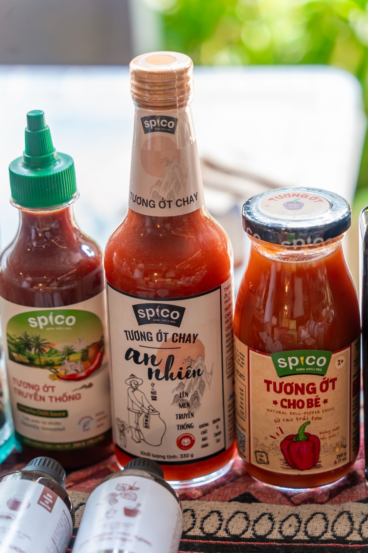 A row of homemade fermented hot sauce bottles in deep red and orange hues on a wooden shelf