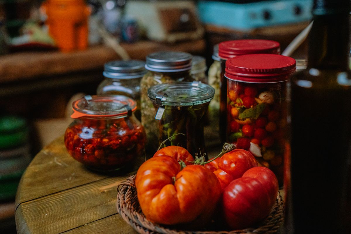 Jars of preserved tomatoes, peppers and vegetables alongside fresh heirloom tomatoes in a rustic kitchen