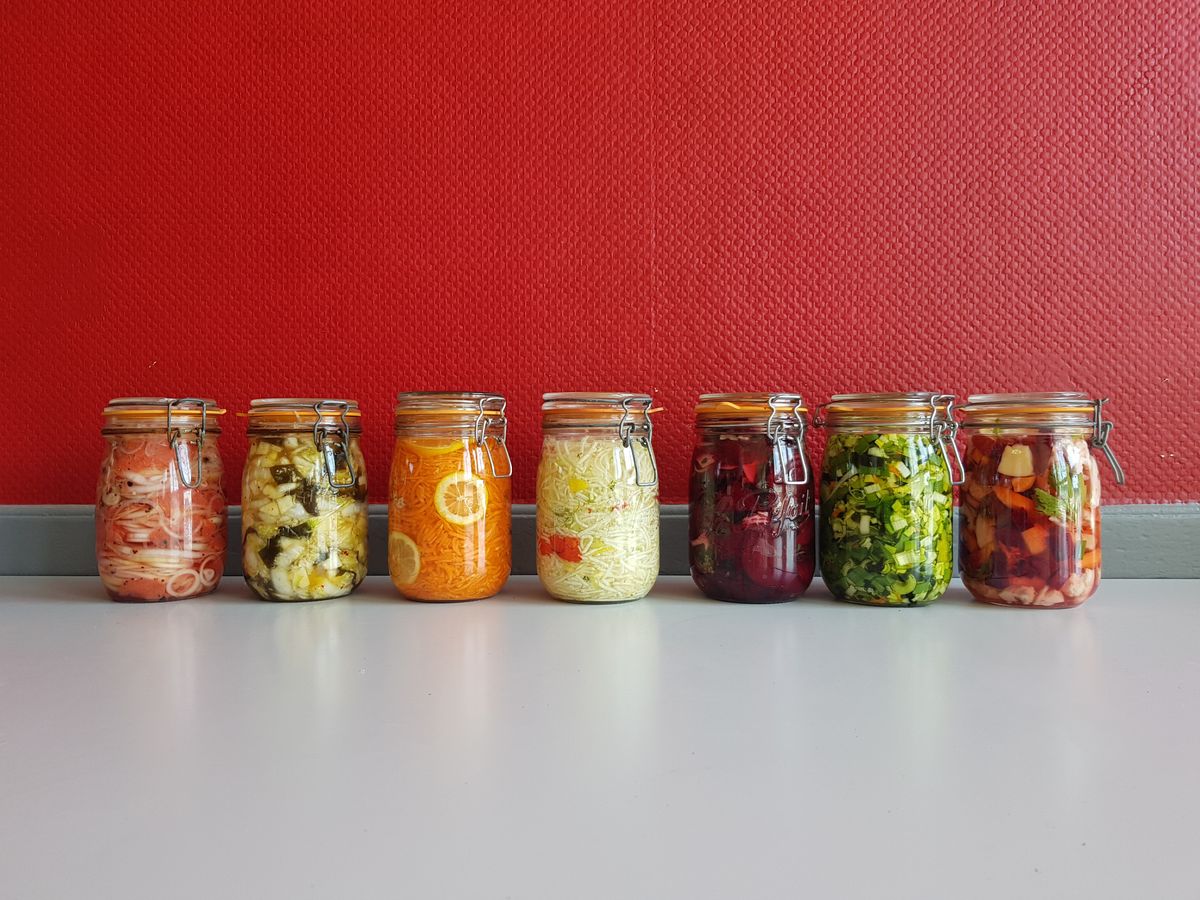 A row of mason jars filled with different fermented vegetables in pink, orange, green, purple and mixed colors