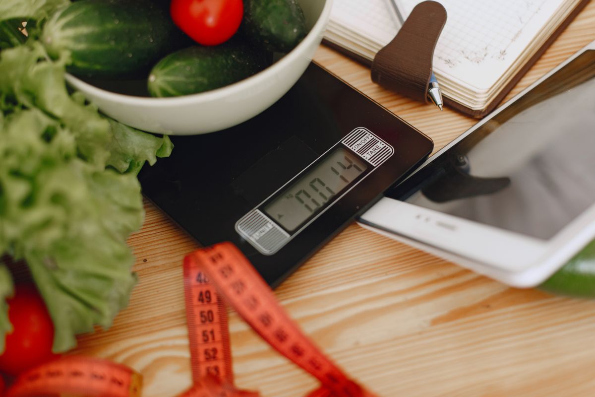 Fresh tomatoes and vegetables in a bowl on a digital kitchen scale, ready for weighing