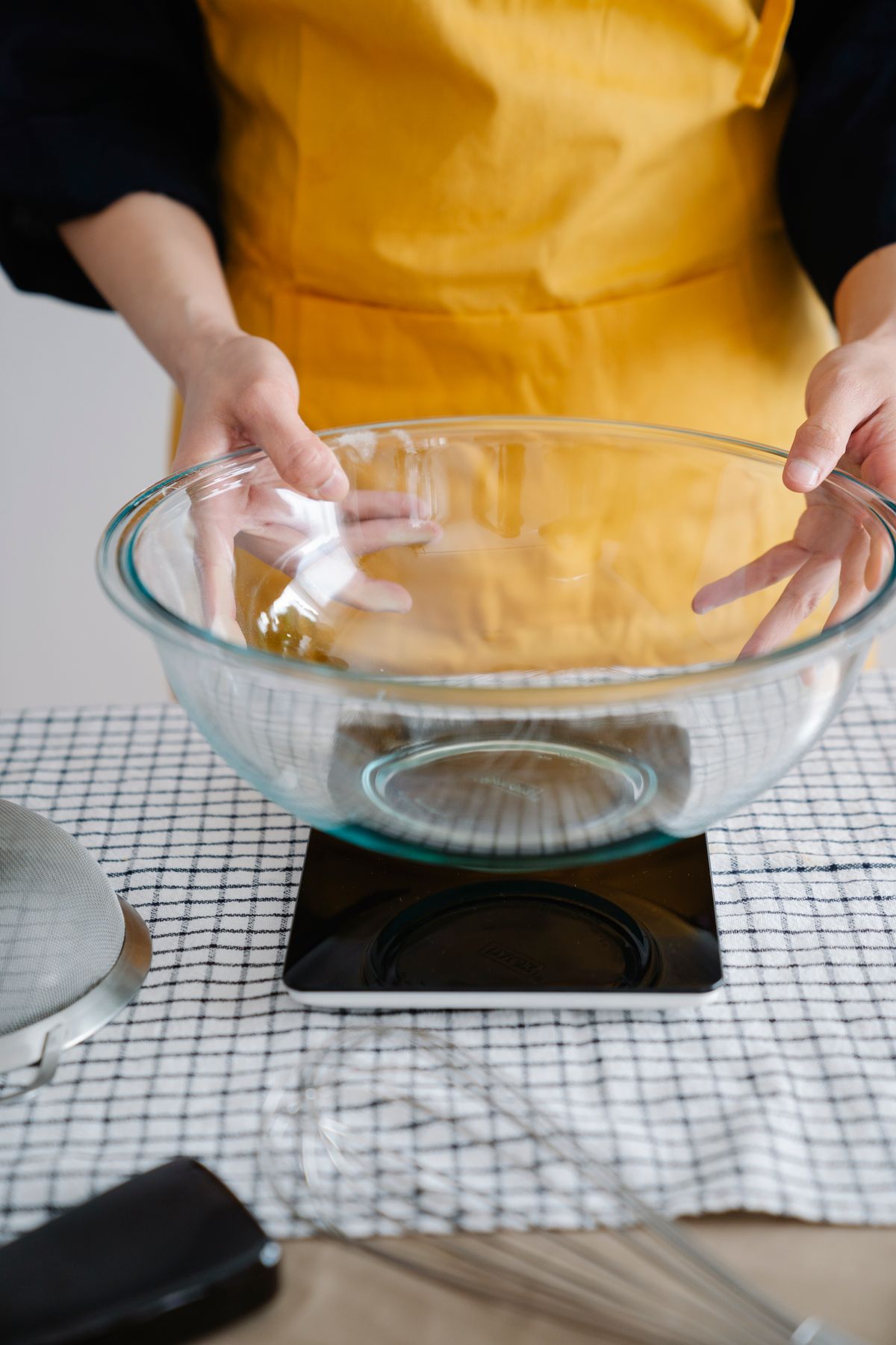 Hands placing a glass bowl on a digital kitchen scale for precise weighing
