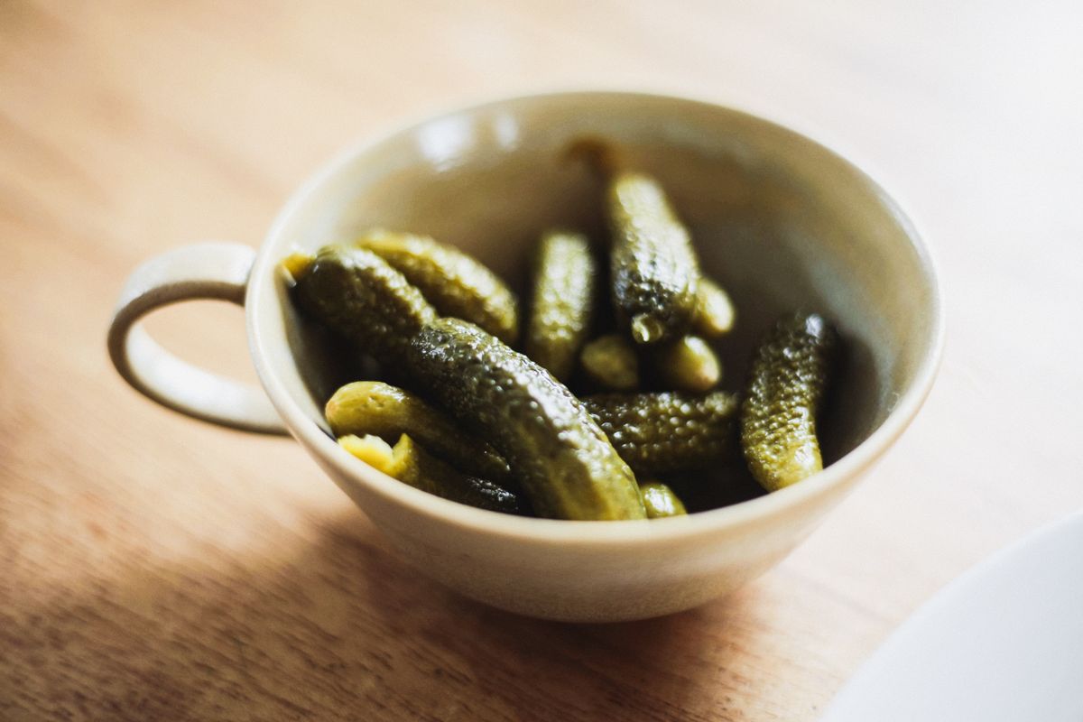 A small ceramic bowl of brined gherkins on a wooden counter